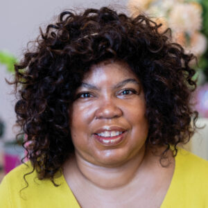 A picture of Red Ladder Artistic Director Cheryl Martin smiling in a bright yellow v neck top
