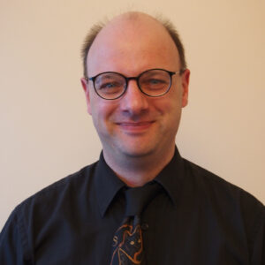 A smiling Tom in black shirt and glasses