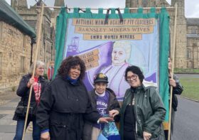 Three women stood in front of a banner reading the daughters of mother Jones
