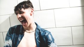 A young man leaning against tiles in a bathroom and screaming