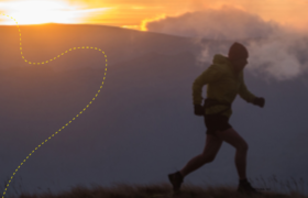 A lone figure running along a fell with the sun setting behind.