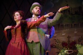 A man and woman in music hall period dress with arms outstretched