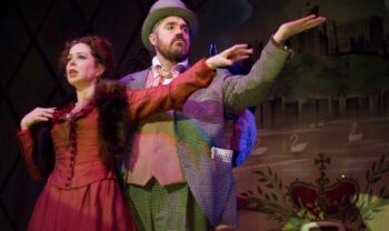 A man and woman in music hall period dress with arms outstretched