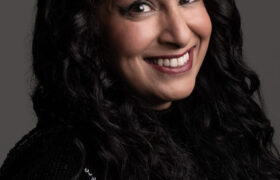 A smiling Seeta against a grey backdrop