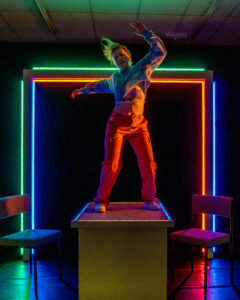 A young woman dancing wildly on a table with a neon frame behind