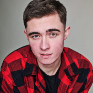 Tyler in red plaid shirt looking directly at camera with half a smile.