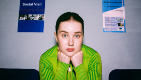 A woman with her face leaning on her fists in a waiting room. On the wall is a poster saying Social Visit
