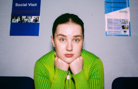 A woman with her face leaning on her fists in a waiting room. On the wall is a poster saying Social Visit