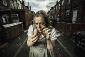 A woman in early 19th century period costume holding an egg and looking devious.