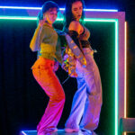 Two young women dancing on a table with neon behind