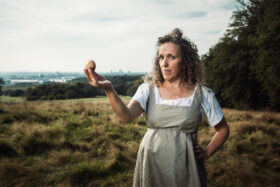 A woman in early 19th century period costume holding an egg