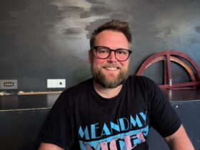 Chris sat smiling in front of a stage block and dark grey wall