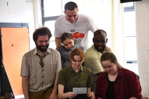 Six people gathered around, reading a letter.