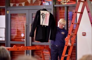 A woman in fire uniform up a red ladder holding up a shirt that reads train for a man's job