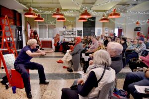 A woman in fire uniform sat on a red chair talking to an audience