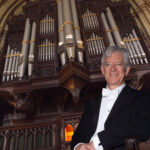 A man in dress suit in front of a church organ