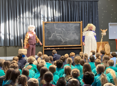Two loopy male professors in drag with a blackboard in front of 400 children